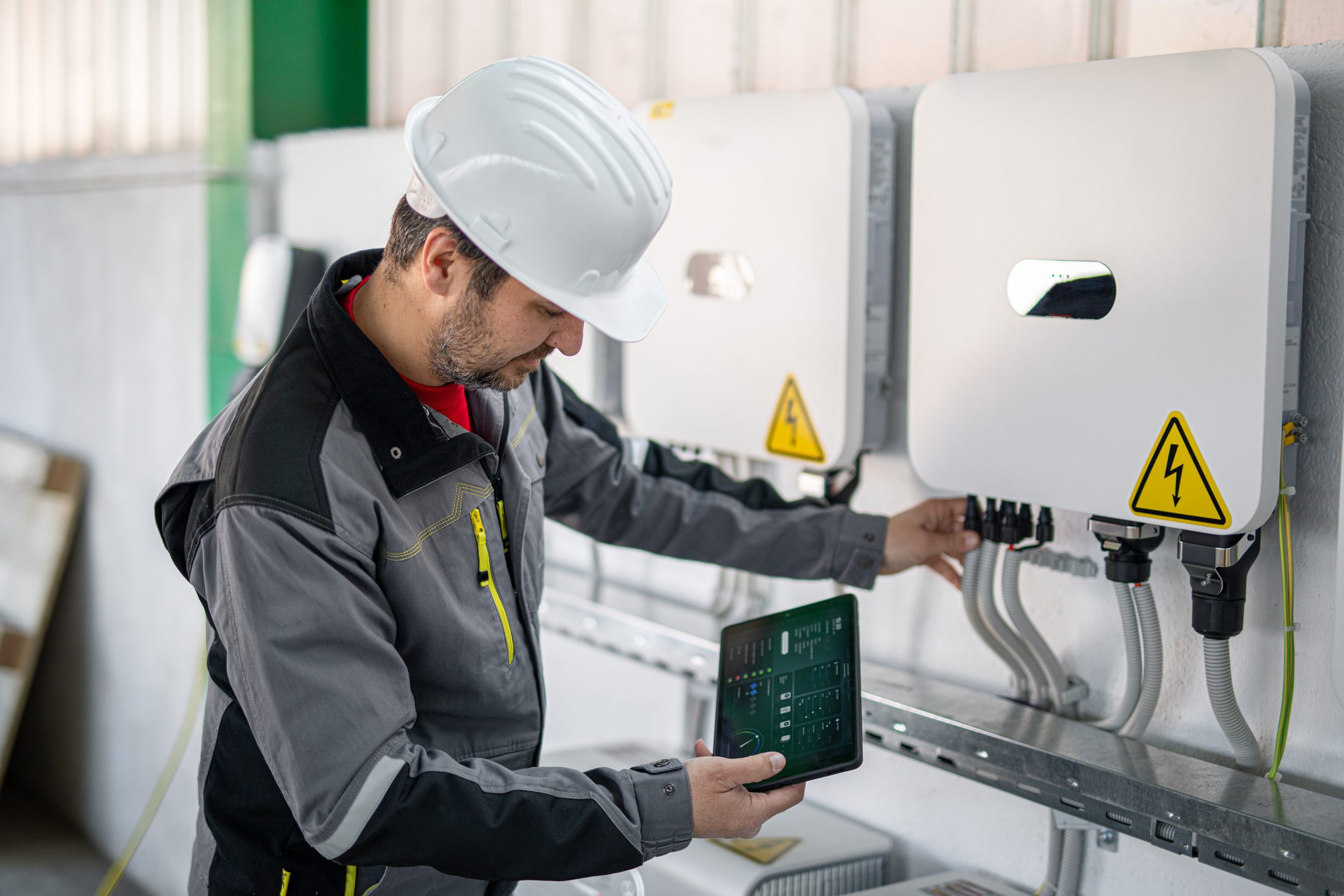 Technician inspecting electrical equipment with tablet.