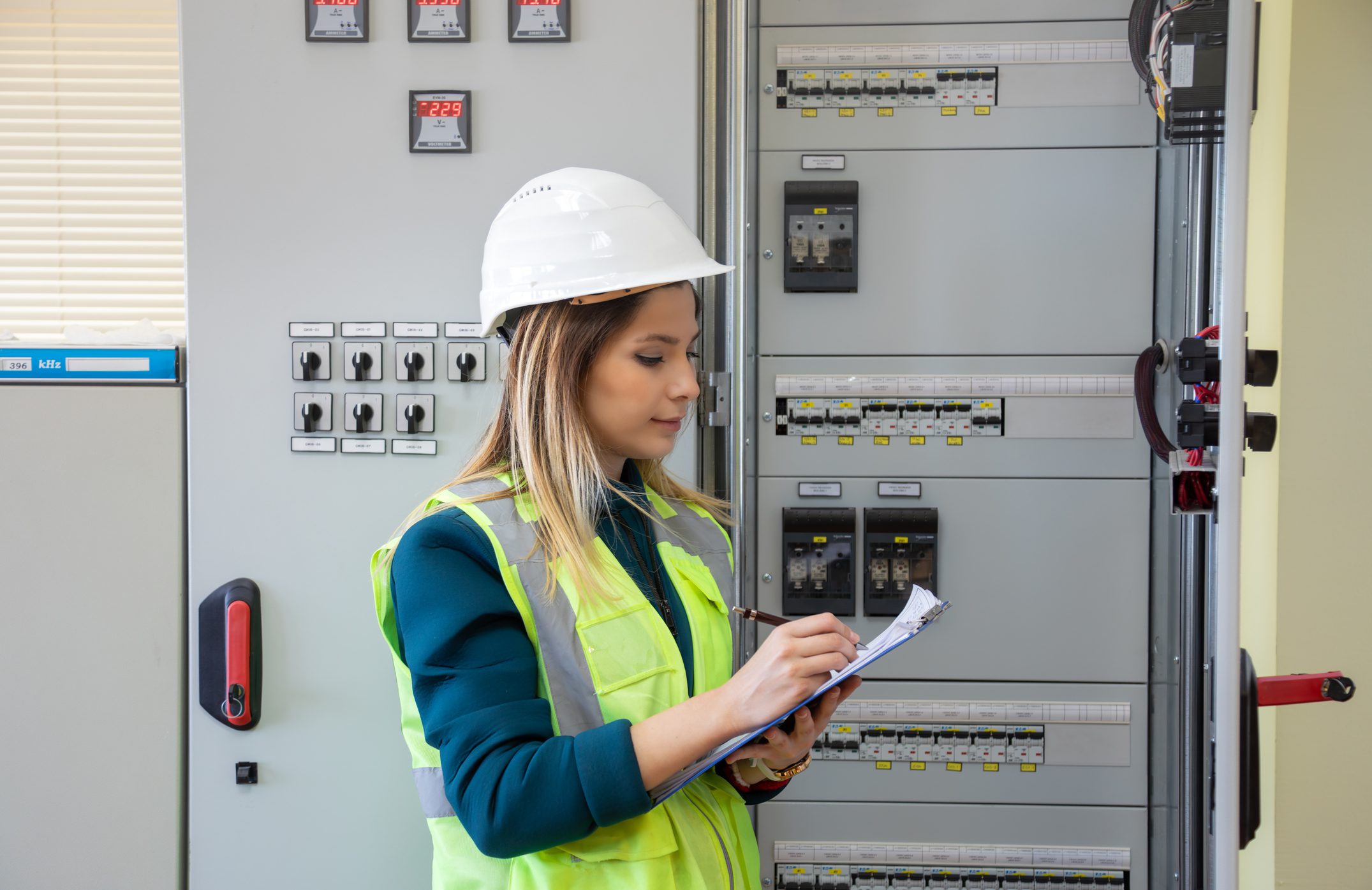 Woman in safety gear checks electrical panel.