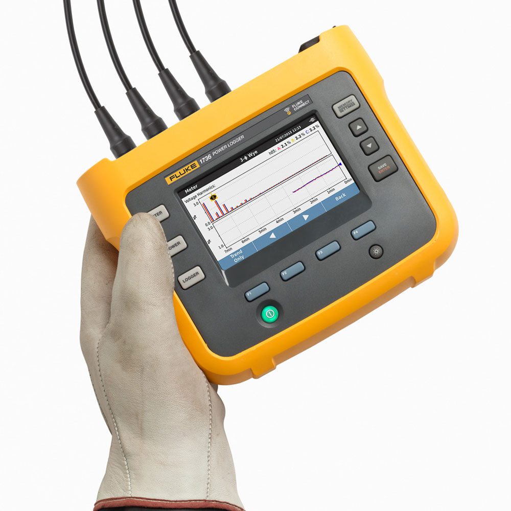 Hand holding a yellow electronic testing device with cables attached.
